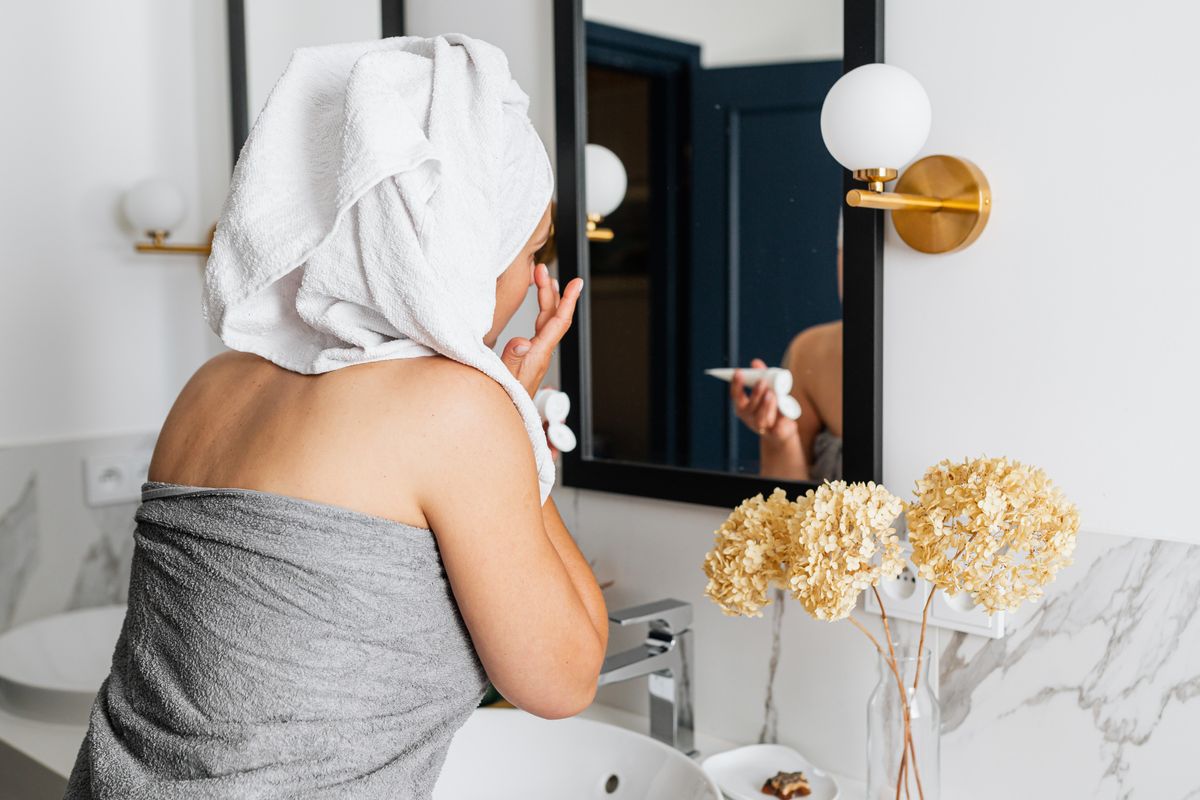A woman applying face cream in front of a mirror